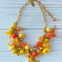 Cute dinosaur charm necklace in bright yellow and orange beads and dinosaur charms. Lenora Dame dinosaur jewelry, handmade jewelry, made in the USA.