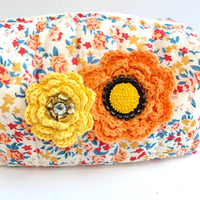 Floral cotton quilted makeup bag for women detailed with yellow and orange crochet flowers with button and rhinestone centers. Small quilted makeup pouch with orange, blue and red floral print.