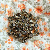 Large six point snowflake shaped rhinestone brooch on a fabric quilted pouch with orange flowers and off white background.