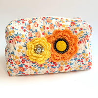 Floral cotton quilted makeup bag for women detailed with yellow and orange crochet flowers with button and rhinestone centers. Small quilted makeup pouch with orange, blue and red floral print.