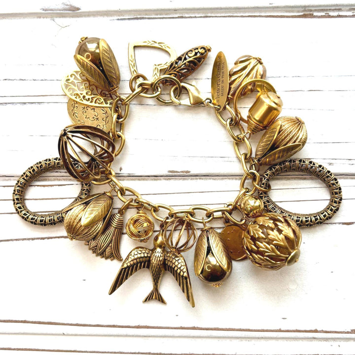 Chunky gold charm bracelet filled with a mix of gold charms in different shapes and sizes hung on a gold cable chain with lobster clasp. Lenora Dame jewelry made in the USA. 