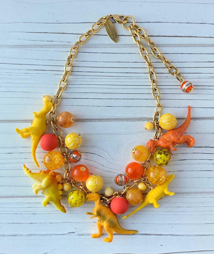 Cute dinosaur charm necklace in bright yellow and orange beads and dinosaur charms. Lenora Dame jewelry for women, handmade jewelry, made in the USA.