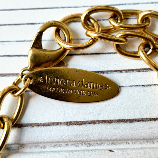 May include: A gold metal chain with a clasp and a tag that reads 'lenora dame* made in the usa'.