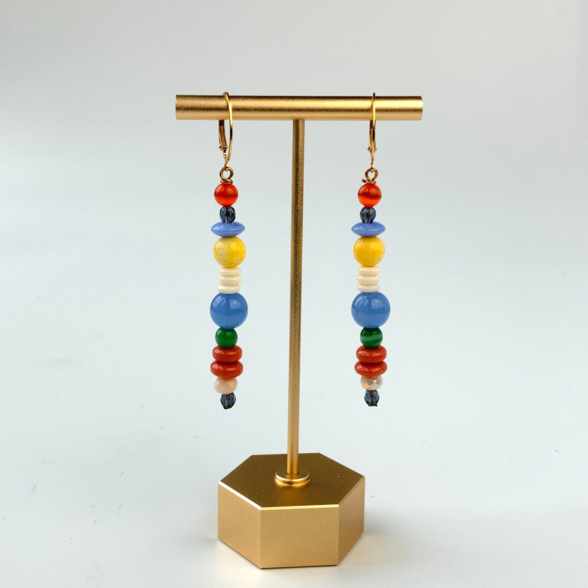 A pair of long skinny earrings with different shaped red, blue, white, and yellow beads. Lenora Dame earrings.