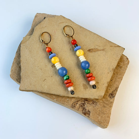 A pair of long skinny earrings with different shaped red, blue, white, and yellow beads. Lenora Dame earrings.
