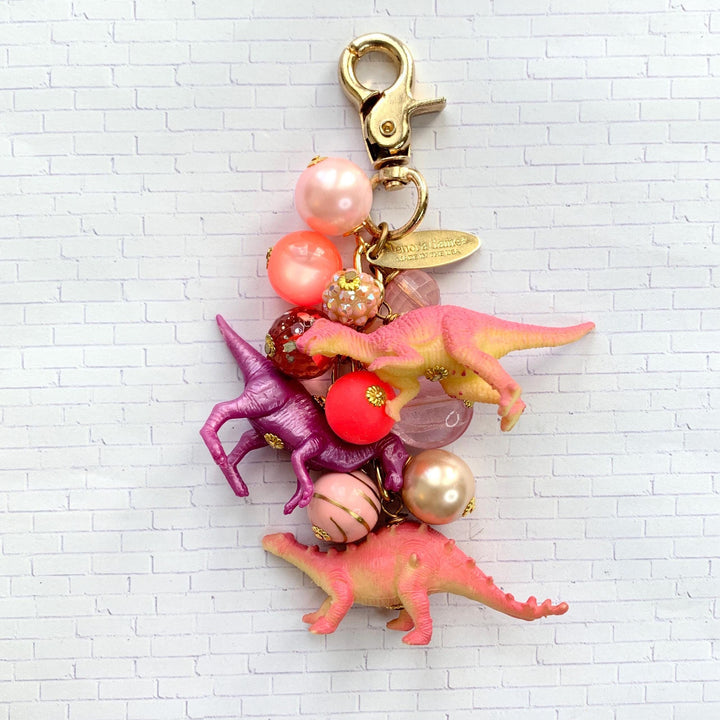 Beaded pink purse charm with three different dinosaur charms. Dinosaur keychain with pink and red beads and three different dinosaur figurines.