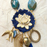 Lenora Dame necklace with metal white lotus mounted on navy blue fabric rosette and a mix of dangling semiprecious stones, brass bird charm and tear drop filigree piece.