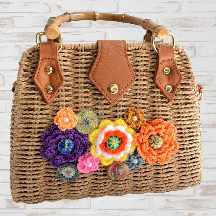 Woven straw handbag for summer embellished with crochet flowers and cloisonne. Wicker handbag with bamboo handle, fabric lining, magnetic snap closure, and removable pu leather strap. Can be converted to a crossbody purse.