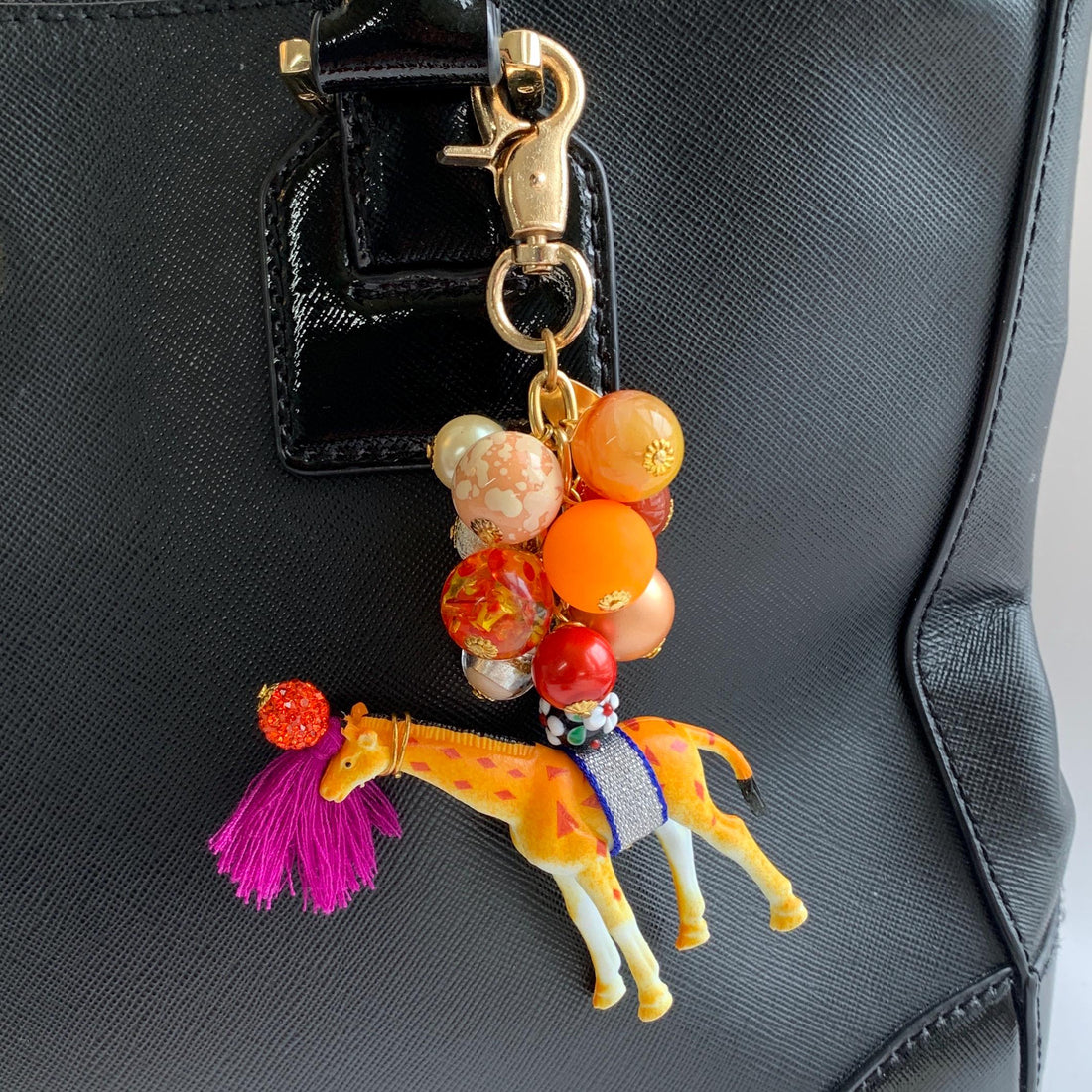 Cute beaded bag charm with embellished giraffe figurine and a mix of beads in orange and red tones and gold tone trigger clasp attached to a purse handle.