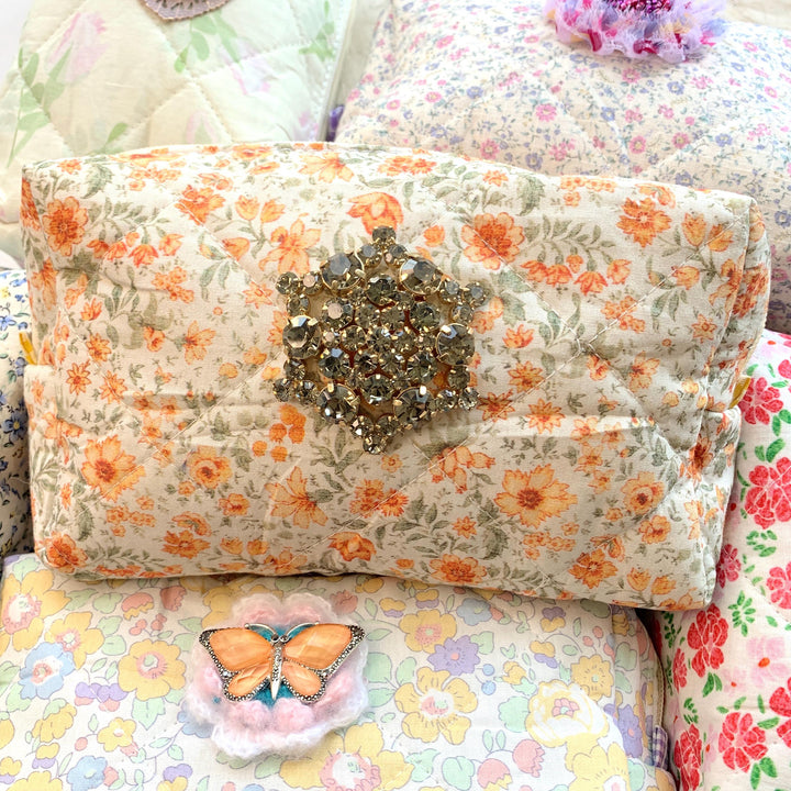 Orange flowers on a cream cotton fabric quilted zipper pouch. Quilted makeup bag embellished with a large star shaped rhinestone brooch. Cute makeup bags with zipper. Gifts for mom.
