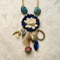 Lenora Dame necklace with metal white lotus mounted on navy blue fabric rosette and a mix of dangling semiprecious stones, brass bird charm and tear drop filigree piece.