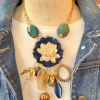Lenora Dame necklace with metal white lotus mounted on navy blue fabric rosette and a mix of dangling semiprecious stones, brass bird charm and tear drop filigree piece.