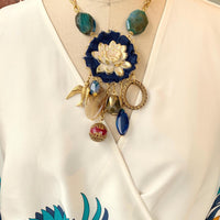 Lenora Dame necklace with metal white lotus mounted on navy blue fabric rosette and a mix of dangling semiprecious stones, brass bird charm and tear drop filigree piece.