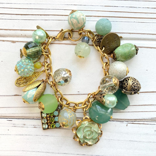 Gold chain charm bracelet filled with assorted green beads and charms hanging from a gold cable chain bracelet. Lenora Dame bracelet. Chunky charm bracelet.