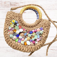 Small half-moon straw bag embellished with a tight collage of flowers, seashells, vintage buttons, large rectangular gemstones, vintage brooches and metal flowers. Rhinestone embellished cute straw bag for summer with top handle and removable shoulder strap or crossbody strap.
