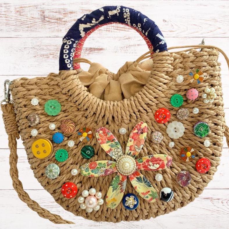 Small half-moon straw bag embellished with buttons, vintage earrings, and large metal flower broach decoupaged in red and yellow floral paper. Cute straw bag for summer with top handle and removable crossbody strap.