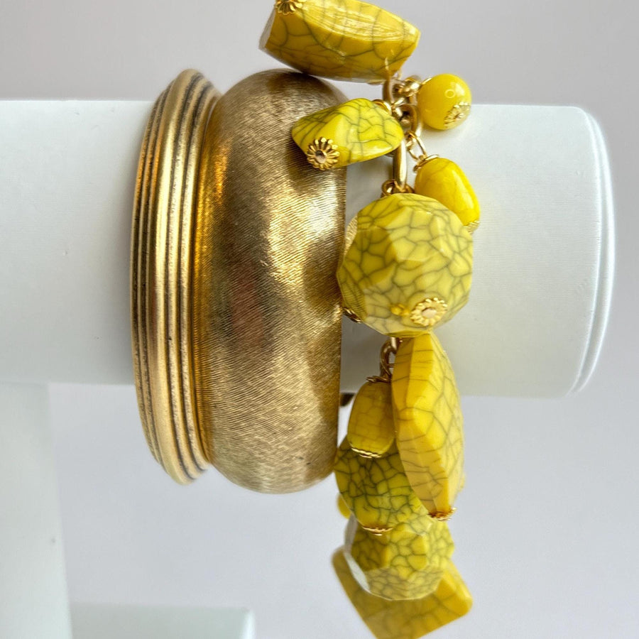 Yellow beaded bracelet for women with square, oval, and round yellow beads with a black crack design wire wrapped on a gold chain shown stacked with two gold bangle bracelets on a white bracelet display arm.