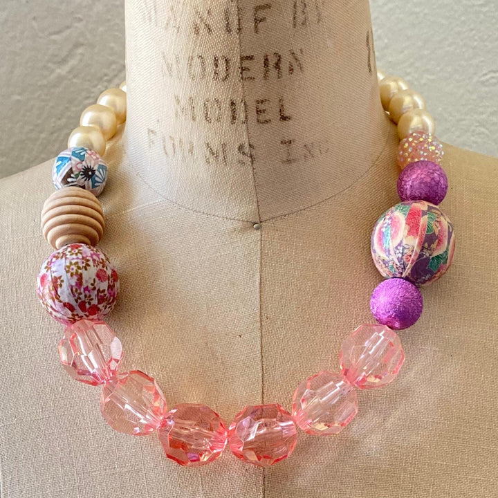 Chunky beaded statement necklace with clear pink beads, purple beads, cream pearls and three wooden beads decoupaged in floral prints. Strung necklace with big chunky beads. Lenora Dame necklace made in the USA.