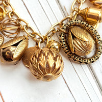 Chunky gold charm bracelet filled with a mix of gold charms in different shapes and sizes hung on a gold cable chain with lobster clasp. Lenora Dame jewelry made in the USA.