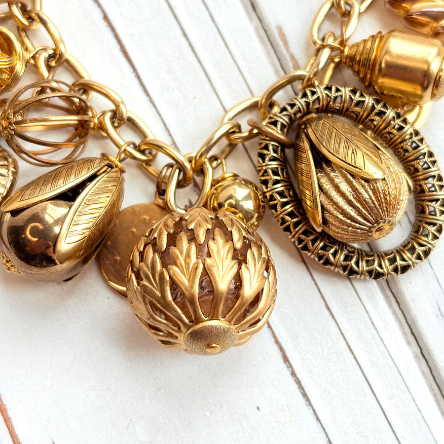 Chunky gold charm bracelet filled with a mix of gold charms in different shapes and sizes hung on a gold cable chain with lobster clasp. Lenora Dame jewelry made in the USA.