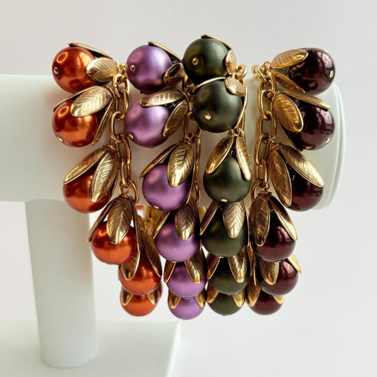 Four gold chain bracelets with pearls encased in gold leaf bead caps. Orange pearl bracelet, matte purple pearl bracelet, matte hunter green pearl bracelet and shiny dark brown pearl bracelet. Lenora Dame bracelets handmade in the USA.