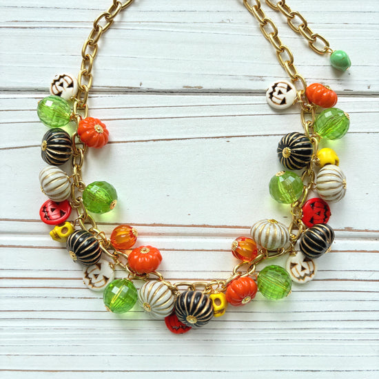 Lenora Dame necklace with a gold chain filled with orange and white jack o lantern beads, orange pumpkins, yellow sugar skull beads, black pumpkins, and green beads. Cute necklace for fall.