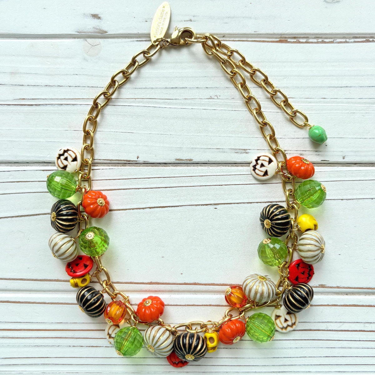 Lenora Dame necklace with a gold chain filled with orange and white jack o lantern beads, orange pumpkins, yellow sugar skull beads, black pumpkins, and green beads. Cute necklace for fall.