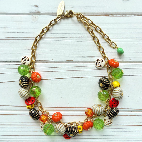 Lenora Dame necklace with a gold chain filled with orange and white jack o lantern beads, orange pumpkins, yellow sugar skull beads, black pumpkins, and green beads. Cute necklace for fall.