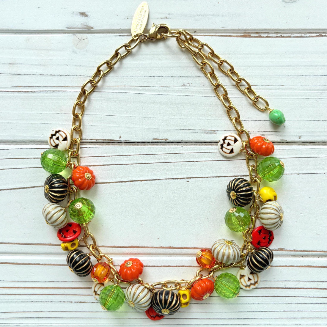 Lenora Dame necklace with a gold chain filled with orange and white jack o lantern beads, orange pumpkins, yellow sugar skull beads, black pumpkins, and green beads. Cute necklace for fall.