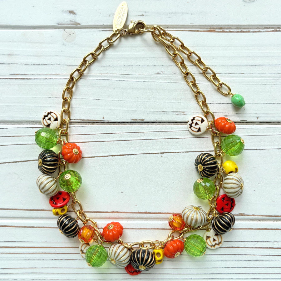 Lenora Dame necklace with a gold chain filled with orange and white jack o lantern beads, orange pumpkins, yellow sugar skull beads, black pumpkins, and green beads. Cute necklace for fall.