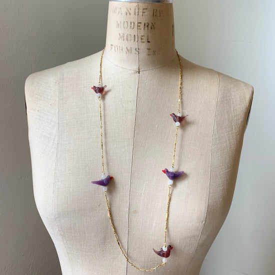 Little purple glass lampworked birds spaced out between bits of gold plated bar chain to create a long necklace. Shown on a vintage dress making form.