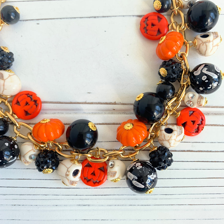 Gold plated cable chain Halloween necklace with orange pumpkins and carved jack-o'-lantern charms, miniature skulls and black and white beads.