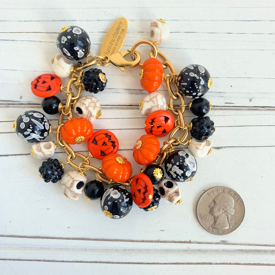Gold plated cable chain Halloween bracelet with orange pumpkins and carved jack-o'-lantern charms, miniature skulls and black and white beads.