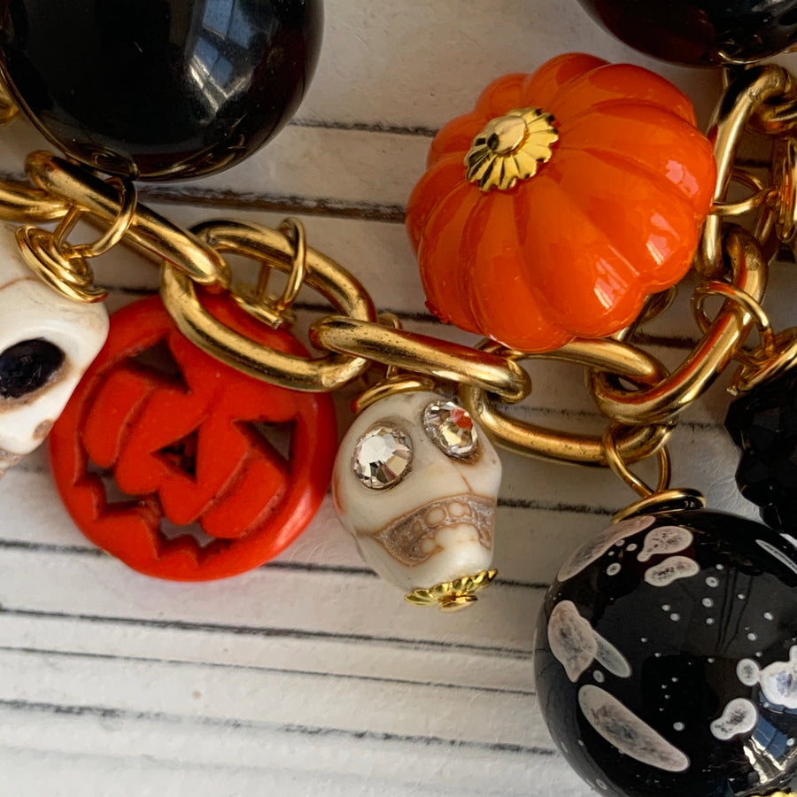 Gold plated cable chain Halloween necklace with orange pumpkins and carved jack-o'-lantern charms, miniature skulls and black and white beads.