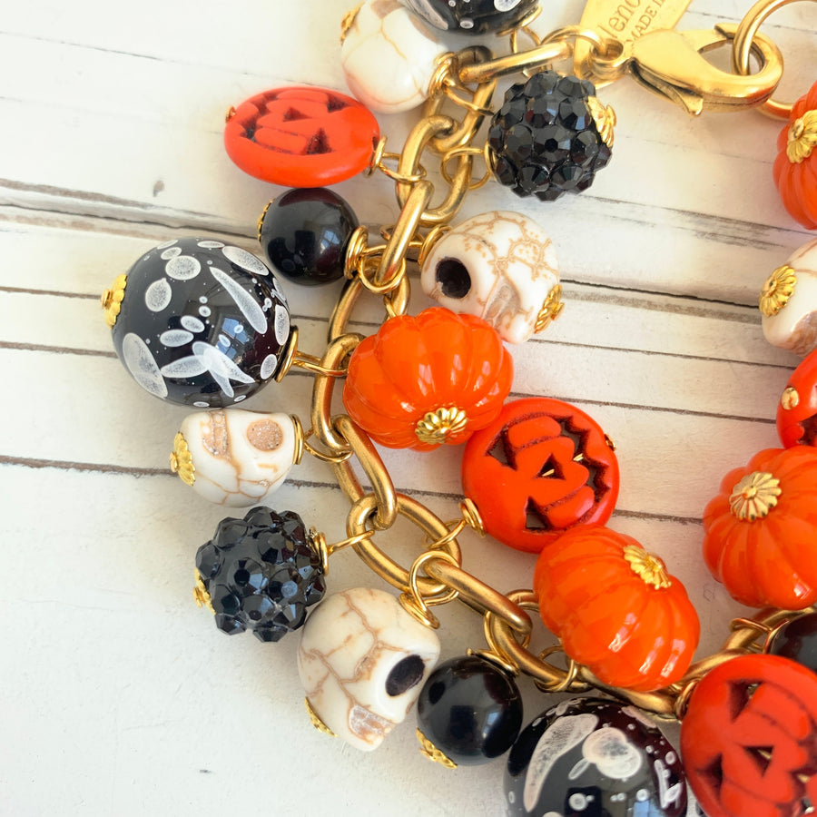 Gold plated cable chain Halloween bracelet with orange pumpkins and carved jack-o'-lantern charms, miniature skulls and black and white beads.